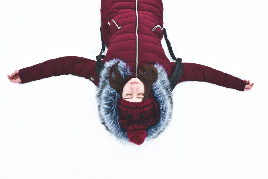 A woman lies on snow with arms open, wearing a red winter coat. Perfect capture of winter tranquility.