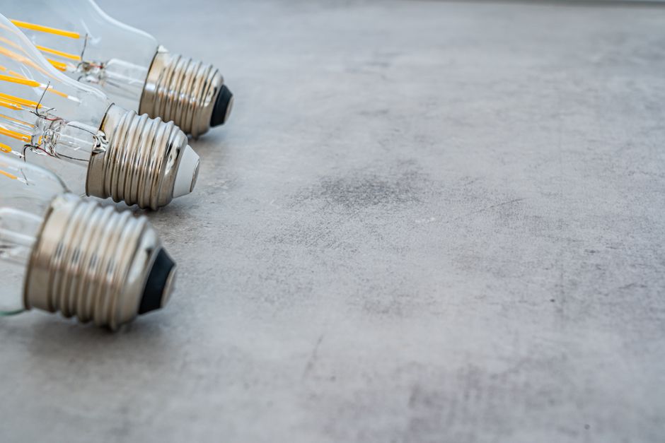 Close-up of glass light bulbs lined up on a gray surface, showcasing their filaments.