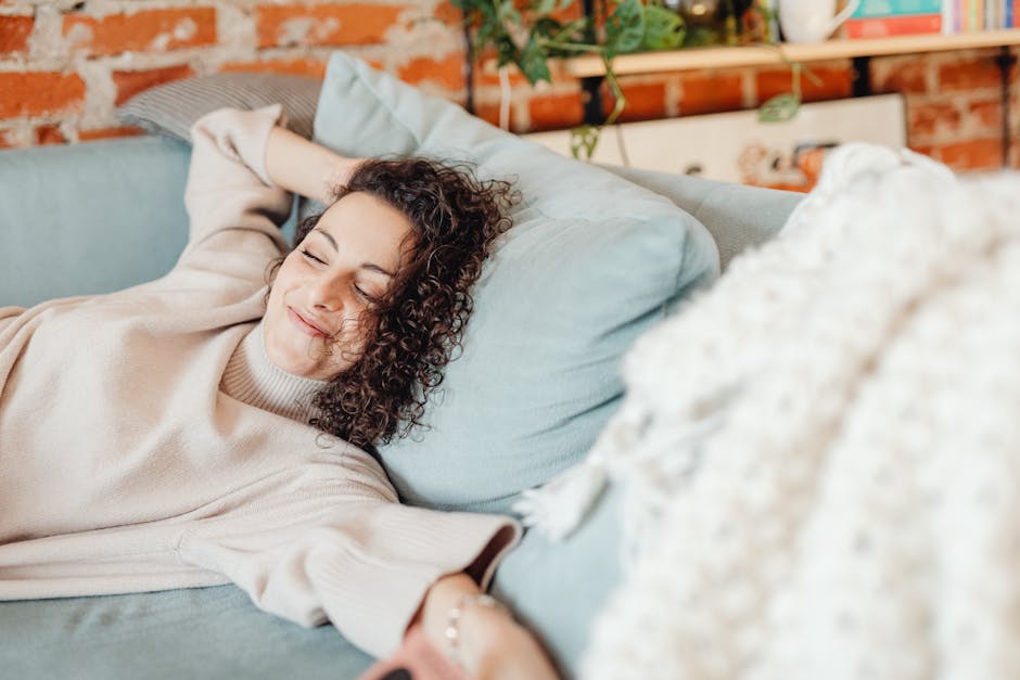 Woman with curly hair relaxing on a comfortable sofa in a cozy indoor setting.