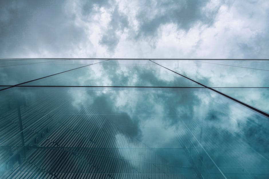 Low-angle view of a modern glass building in Oslo reflecting a cloudy sky, creating a striking urban scene.