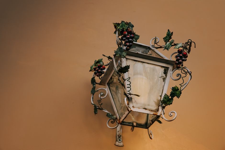 Vintage wall lantern adorned with grapevine decorations on a peach wall, offering rustic charm.