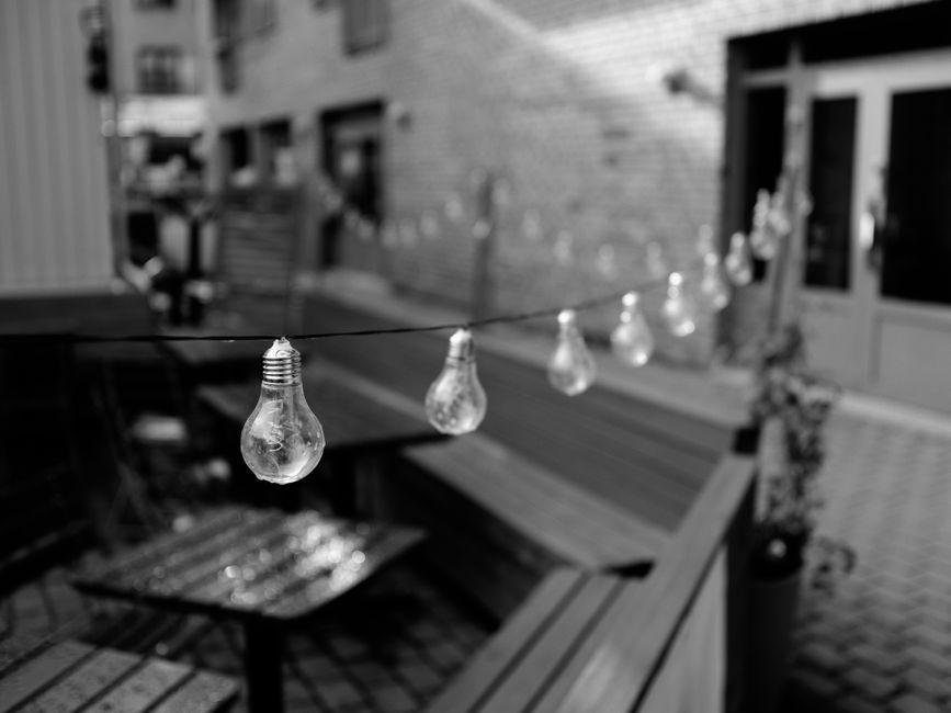 Black and white close-up of string light bulbs in an Oslo courtyard.