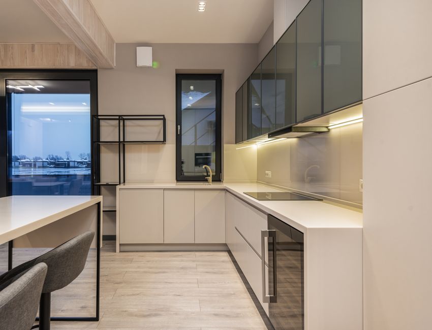 Minimalist white furniture and table with soft chairs in spacious kitchen with modern appliances and parquet floor in villa