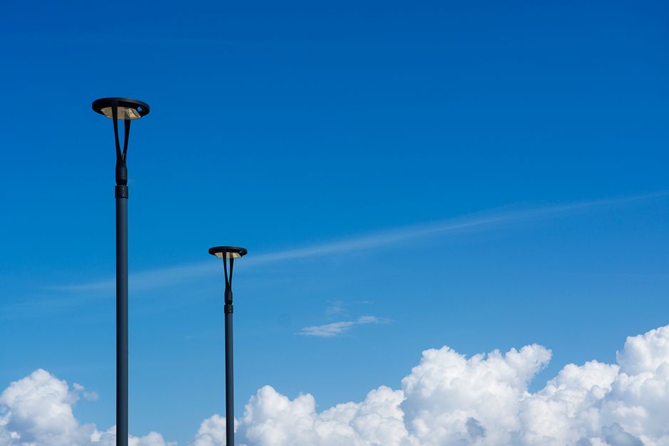 Modern streetlights set against a vibrant blue sky with fluffy clouds.