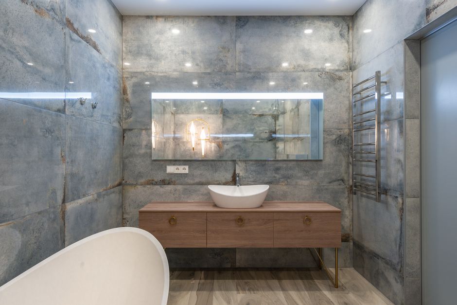 Creative design of bathroom with washstand on cabinet under mirror on stone wall against bathtub in house