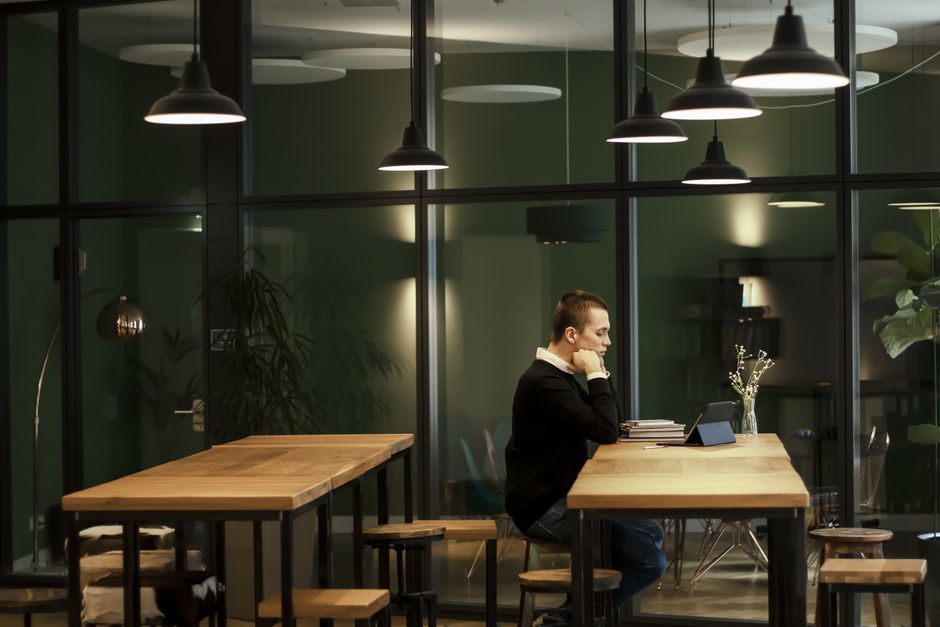 Man focused on work at a modern office with wooden tables and glass panels.