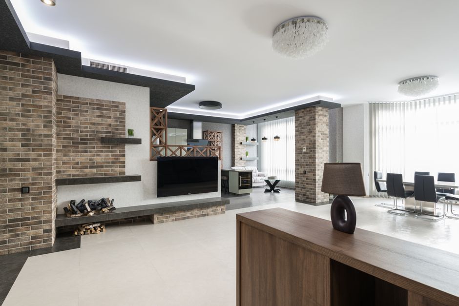 Modern TV at decorated wall in spacious living room with wooden cupboard in light apartment with table near big window