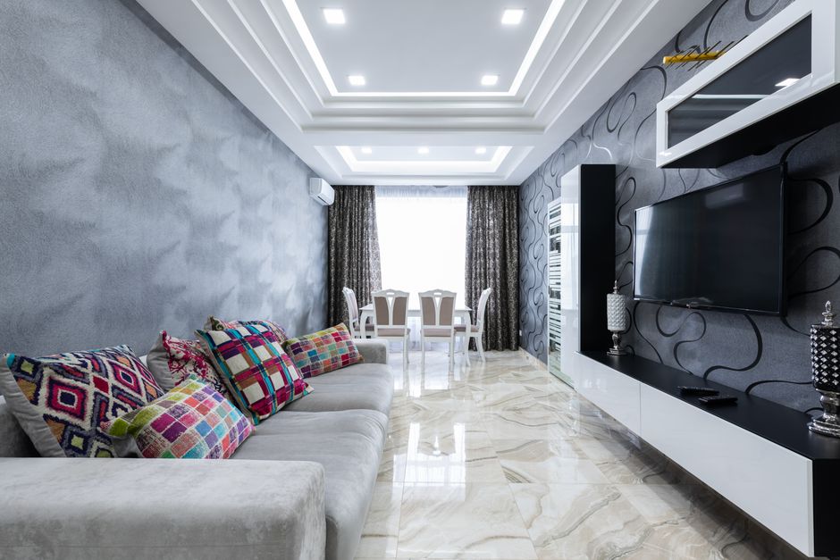 Comfortable gray sofa with colorful pillows placed in front of TV in stylish living room with gray walls in luxury apartment