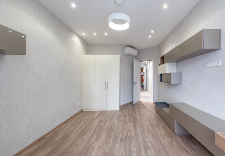 Interior of spacious light room with bright lamps and white wardrobe placed at wall and modern cabinets near opened door