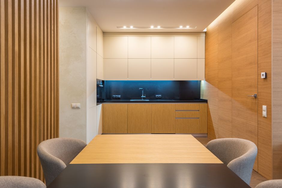 Spacious kitchen with illuminated cooking zone near wooden cabinets and soft chairs around table