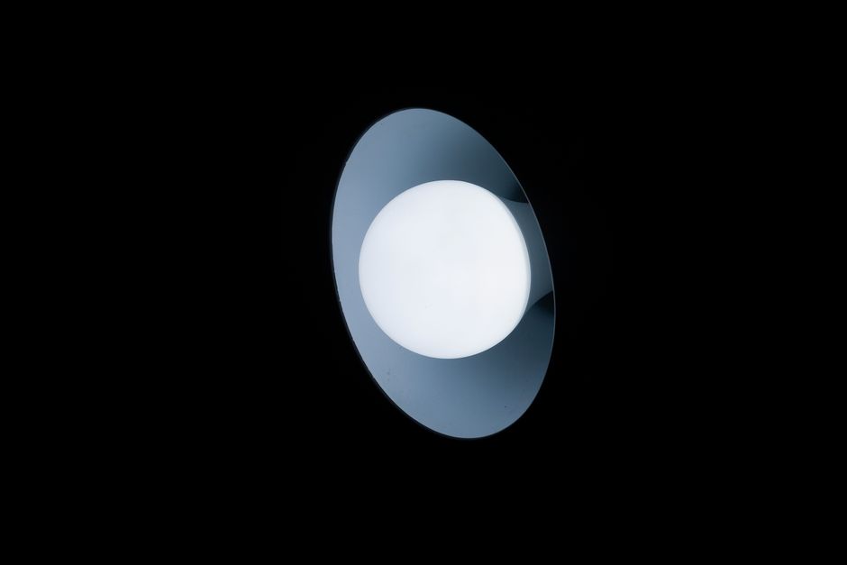 A minimalist circular overhead light emitting a soft glow in a dark room, highlighting contrast.