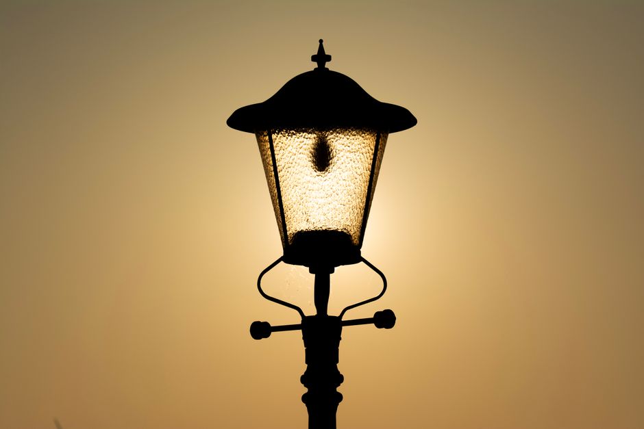 Silhouette of a vintage lamp post illuminated by the warm glow of a sunset.