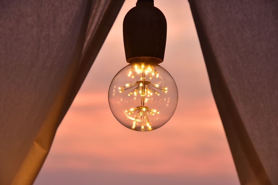A close-up of an Edison bulb glowing warmly against a soft pink sunset sky.