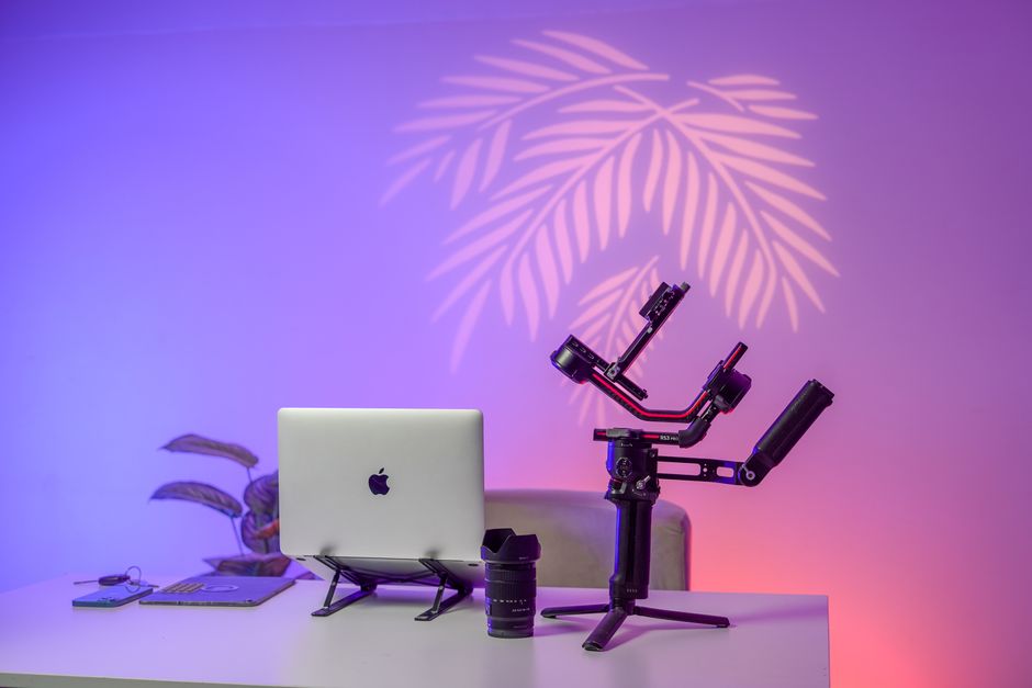 A stylish desk setup featuring a laptop, camera gimbal, and colorful lighting for creative workspaces.