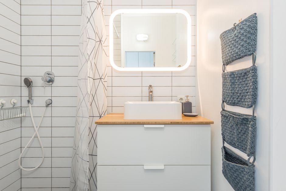 Illuminated mirror hanging on tiled wall over white ceramic sink near shower cabin in minimalist bathroom