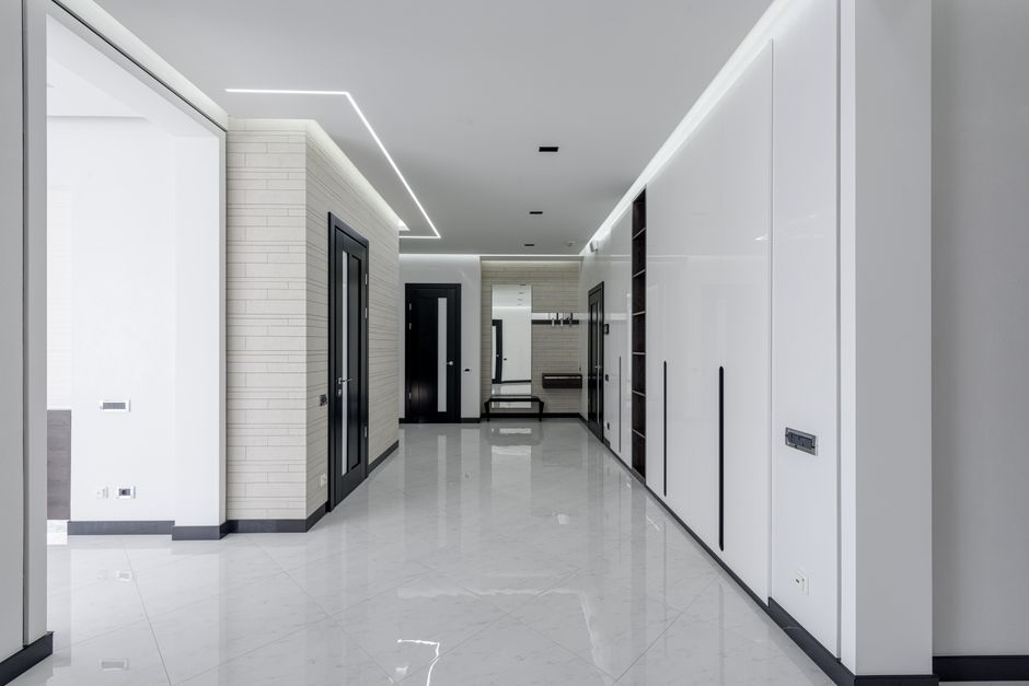 Spacious corridor of modern apartment with white walls dark doors and LED highlighting on ceiling