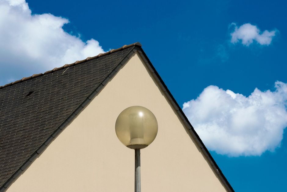 A contemporary building roof with a streetlamp set against a bright blue sky with scattered white clouds.