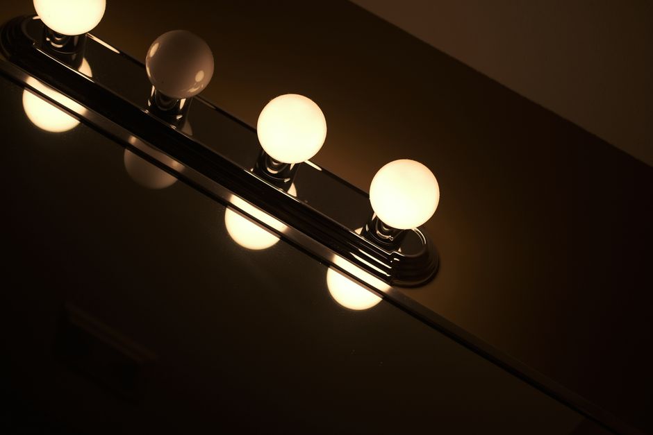 Contemporary bathroom light fixture with glowing bulbs reflecting off a mirror.