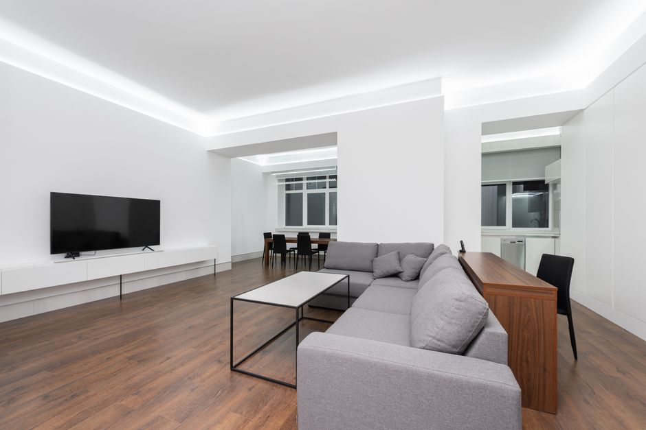 Wooden table near comfortable sofa against white wall with black TV in light modern living room with windows at home