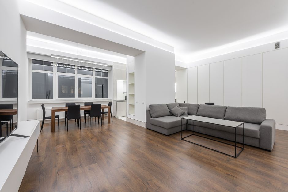 Comfortable couch placed against TV near wooden table with chairs in modern apartment with minimalist interior and partition at home