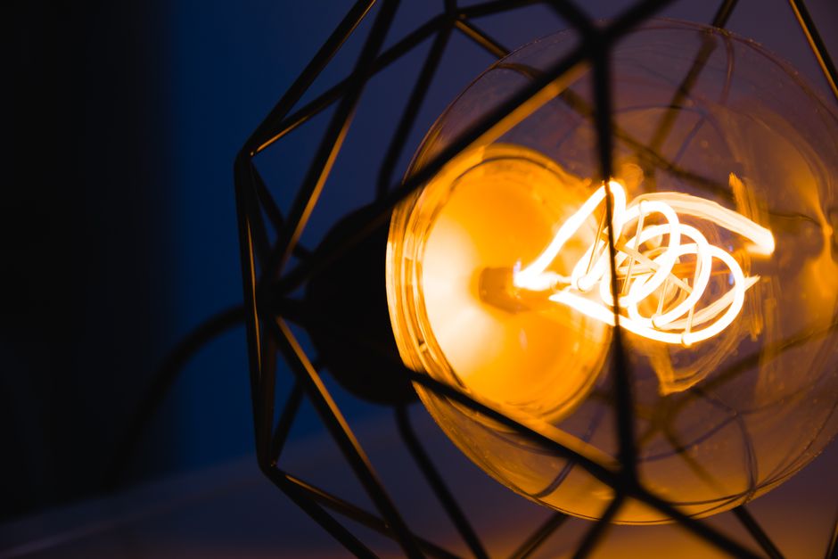 A glowing light bulb captured in a metal geometric frame, illuminating its surroundings.
