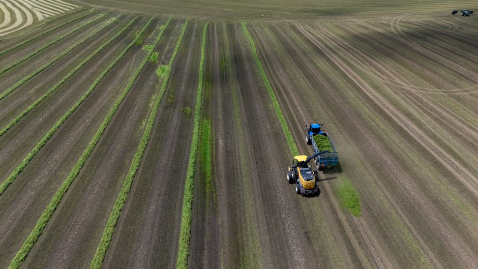 Aerial shot capturing a tractor harvesting crops in a vast farm field during the daytime.