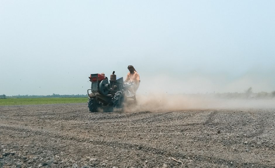 A farmer operates a tractor to plow a dusty field in Pabna, Bangladesh, capturing rural agricultural life.