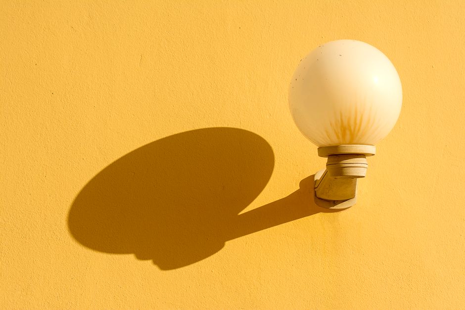 Close-up of a round lamp casting a distinct shadow on a vibrant yellow wall.
