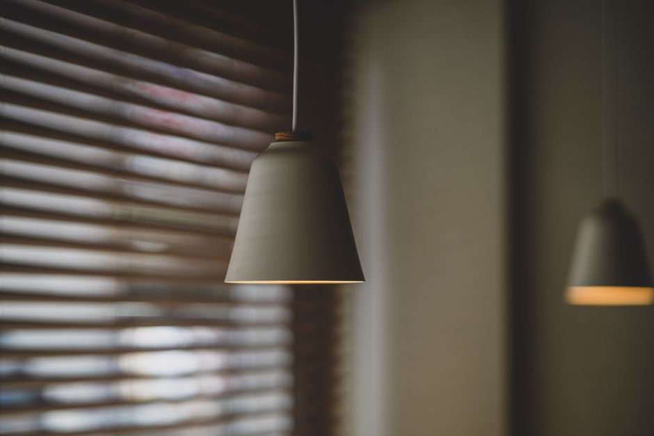 A minimalist pendant light against a soft focus background with window blinds.