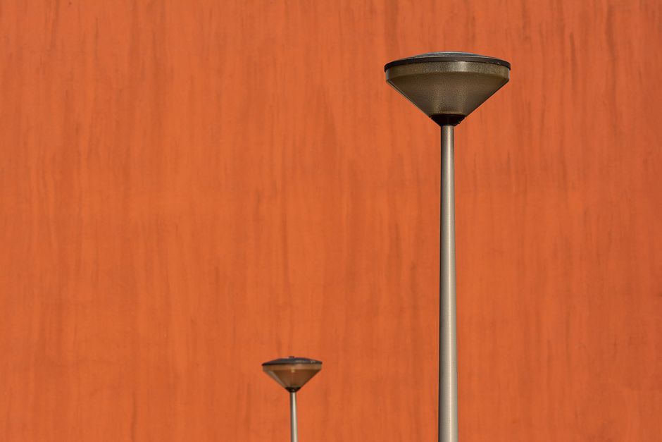 Two modern street lamps against a vibrant orange textured wall in a minimalist setting.